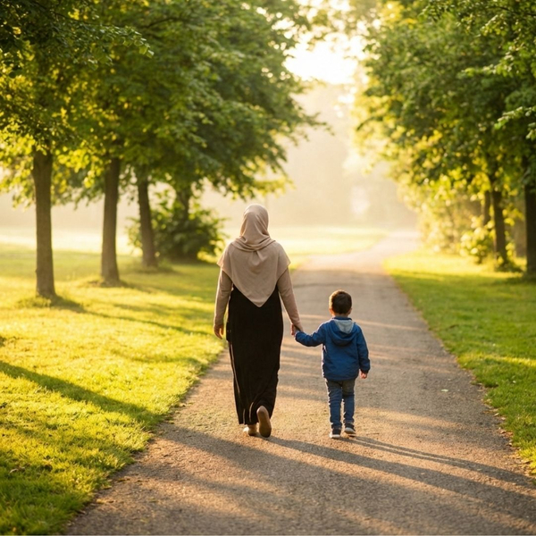 A mother and young child holding hands while walking together down a sunny park path.