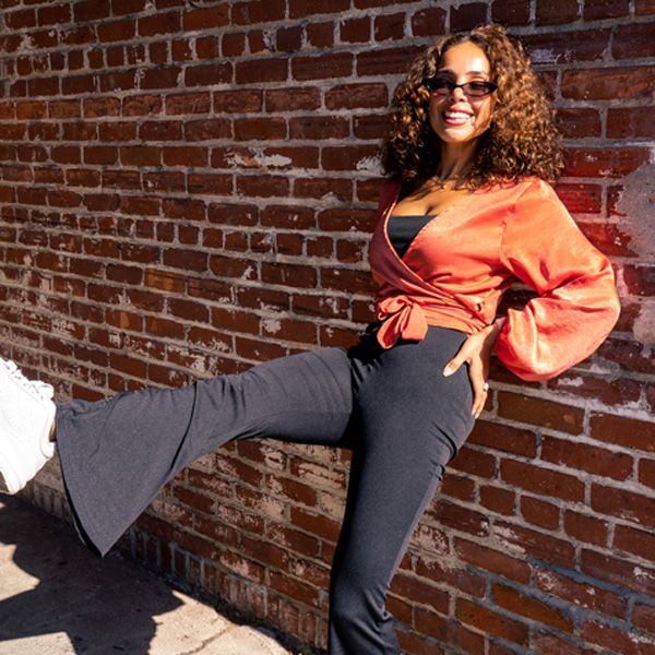 dalia in flared pants against brick wall, kicking leg out