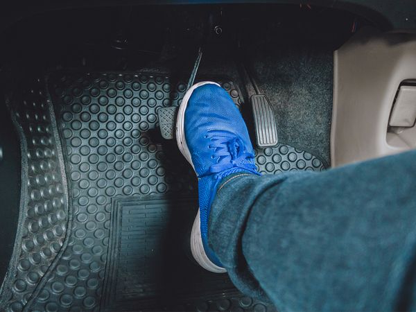 Foot wearing blue sneaker hitting brake pedal