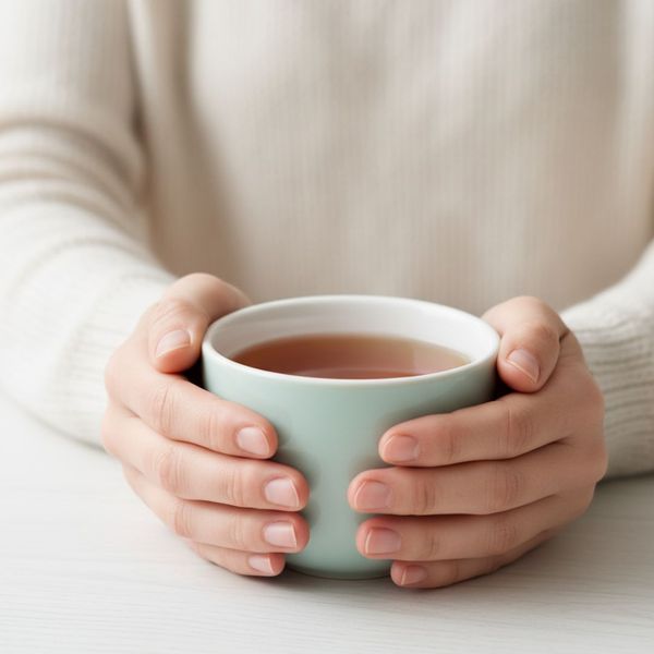 A person's hands gently holding a warm mug of tea. A person's hands gently holding a warm mug of tea.