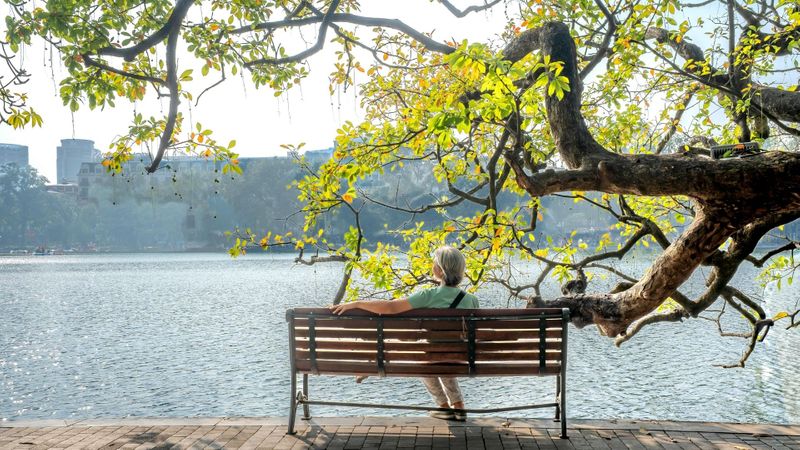 A woman sitting on a bench near a river. A woman sitting on a bench near a river.