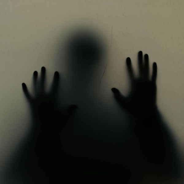 shadow of a figure with hands against the glass