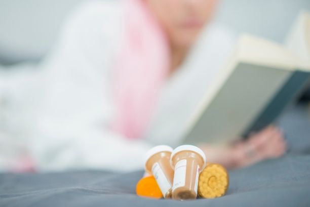 bottle of pills in front of a patient reading a book