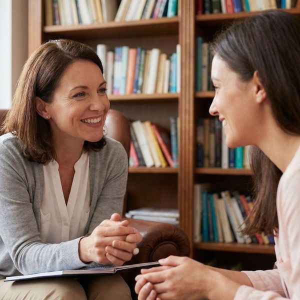 A close-up of a smiling therapist and client in a cozy, book-lined room.