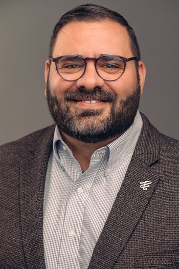 Smiling man with glasses, button down shirt, and suit jacket