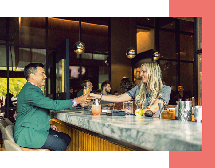 A female bartender at a hotel handing a guest his drink