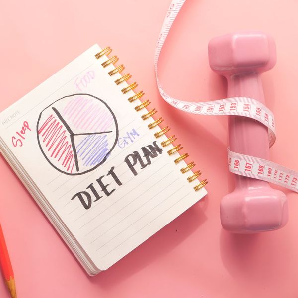 Notebook that says "diet plan" with a pie chart, sitting next to a pink weight and measuring tape. 