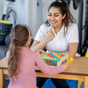 a woman sitting across from a little girl, smiling and teaching her speech sounds