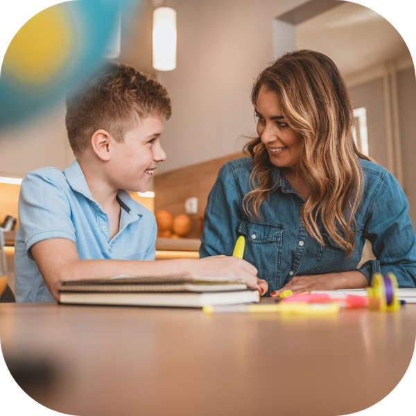 a woman sitting at a table with a young boy with school supplies in from of them