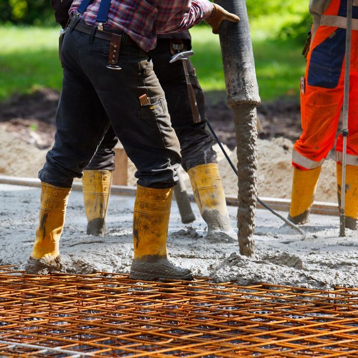 An image of a construction crew pouring concrete for a foundation, with rebar in the foreground. An image of a construction crew pouring concrete for a foundation, with rebar in the foreground.