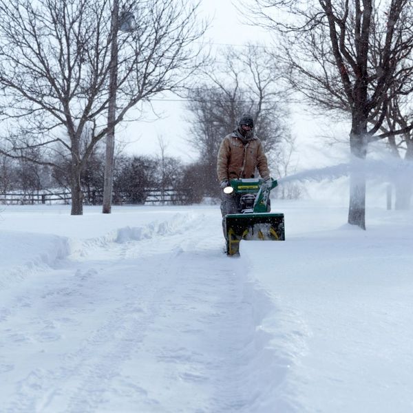a man using a snow blower in street
