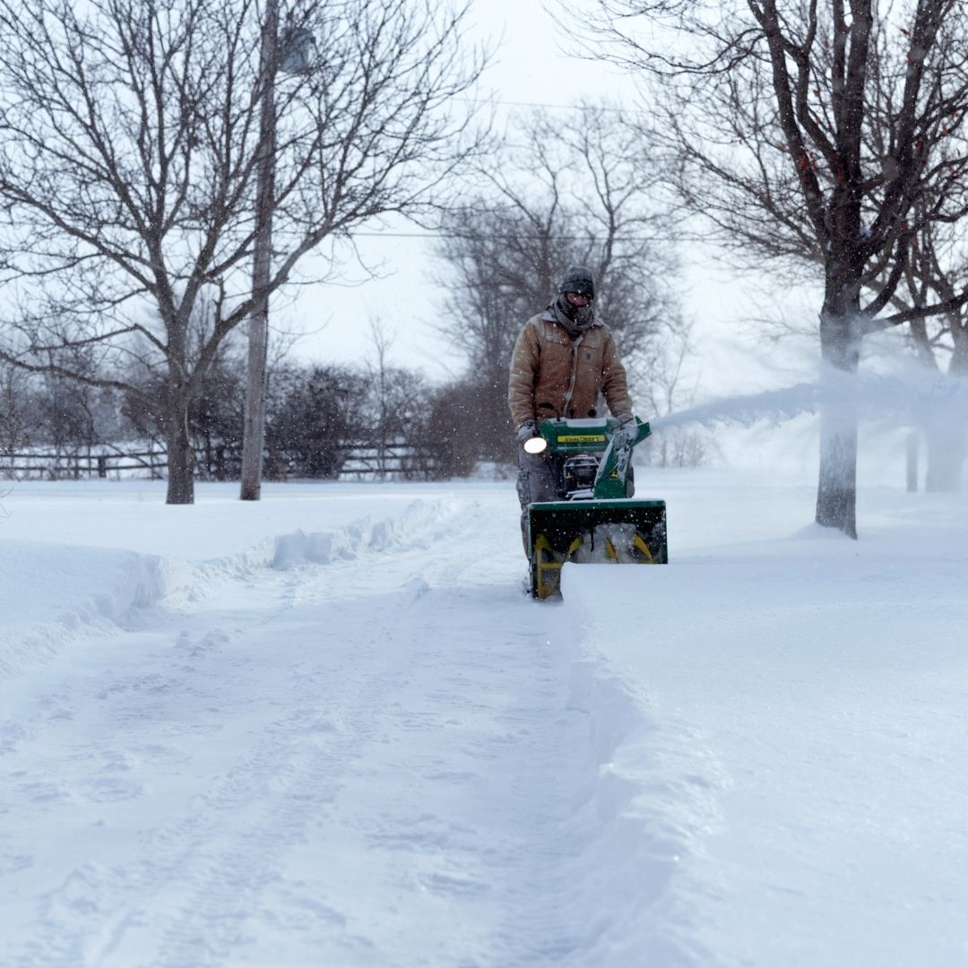 a man using a snow blower in street