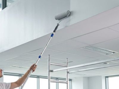 A painter using an extended paint roller to paint the ceilings of a commercial building