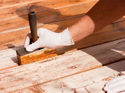 A person staining a wooden deck with a brush 