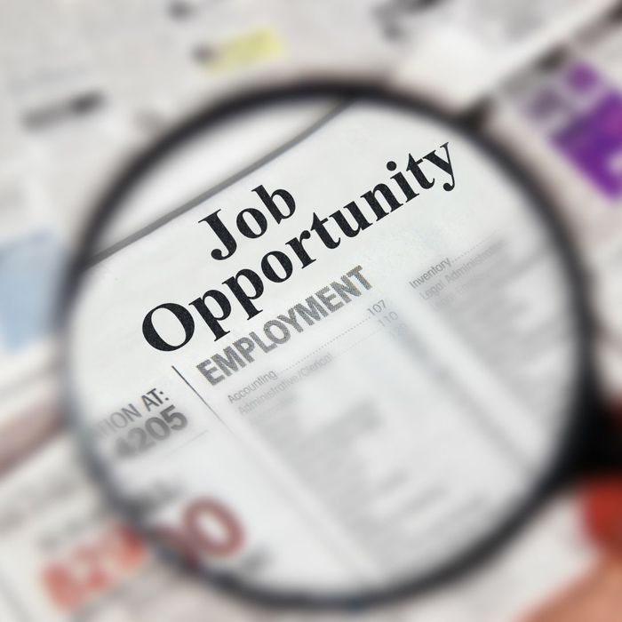 person putting a magnifying glass up to a newspaper with the words "Job Opportunity" at the top. 