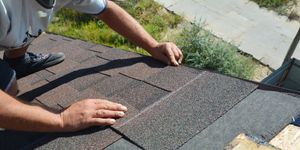 person installing shingles on roof