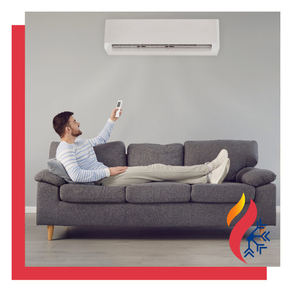 A man sitting on a couch using a remote to control a mini-split AC system