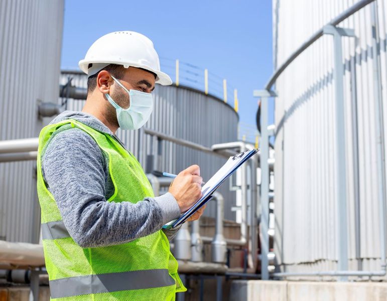 Image of worker with hardhat, mask, safety vest and a clipboard