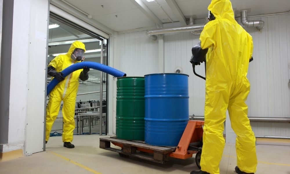 workers in hazmat suits moving barrels of chemicals