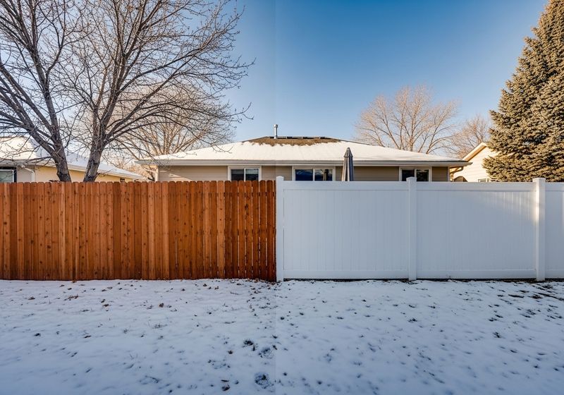 A side-by-side comparison of a wood and vinyl fence in a snowy Denver backyard.