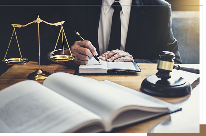 a lawyer taking notes and looking at a book while sitting at a desk with a gavel and the scales of justice