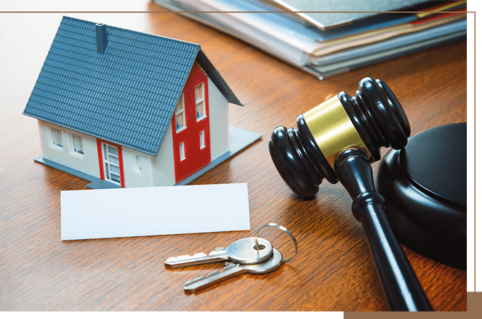 a toy house with keys on a desk with a gavel and paperwork