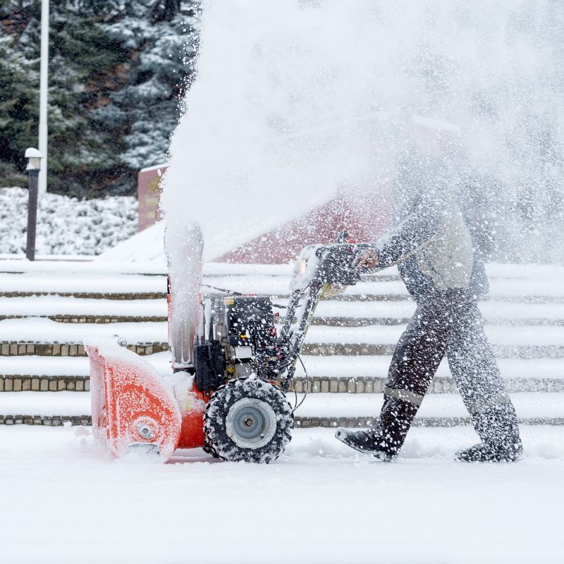 Worker pushing snow blower at business Plowing sidewalk snow