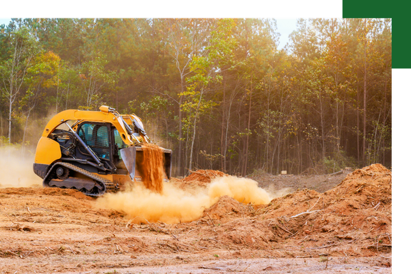A yellow compact track loader performing soil conditioning and grading on a cleared land site during sunset to prepare for new construction.