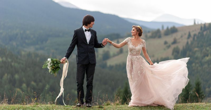 a couple in wedding attire posing in front of mountains