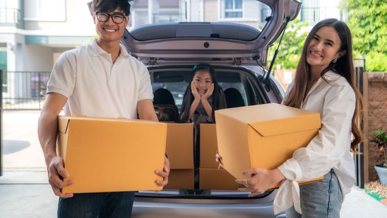 Family holding moving boxes by car
