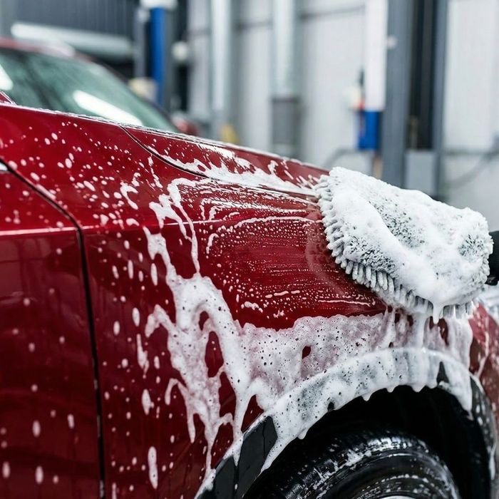 Close-up of a deep red vehicle's paint covered in rich car soap suds during a professional hand wash.