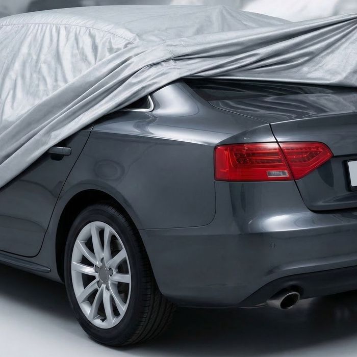 Rear view of a dark grey car half covered by a soft, breathable fabric car cover in an indoor storage unit.