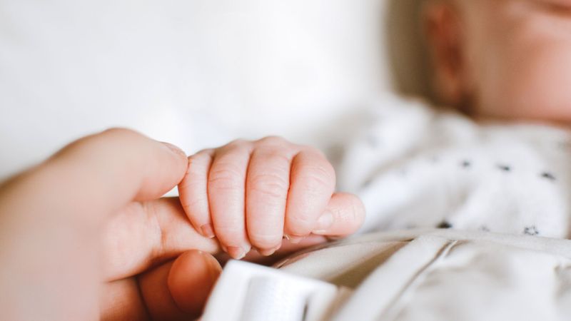 A mother holding a newborn's hand.
