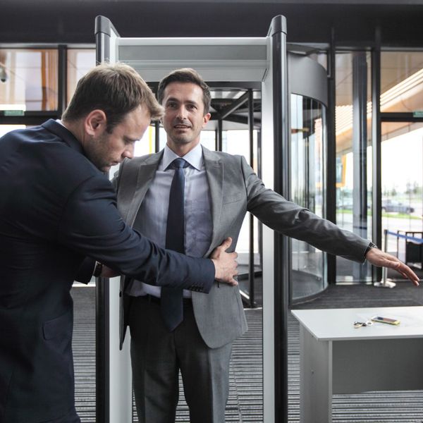 a security guard patting down a person entering through a metal detector