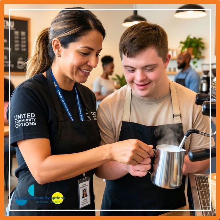 A female job coach guiding a young man as he learns to steam milk for a latte in a community cafe.