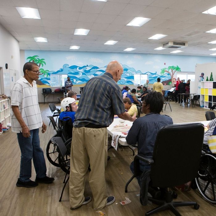 Participants and staff interacting during a group activity at a UCO Day Services center, featuring a bright mural of a beach scene on the wall.