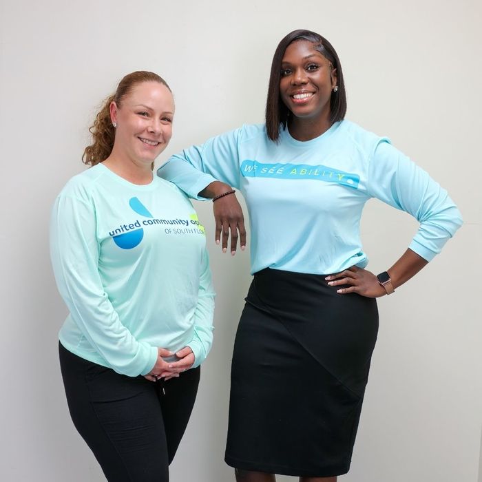 Two smiling UCO female staff members standing side-by-side; one wears a shirt with the UCO logo, and the other wears a shirt reading, "We See Ability."
