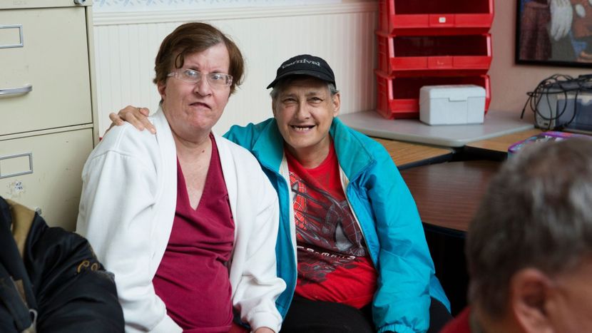 Two adults smiling and sitting close together, with one person's arm draped over the other, showing friendship and belonging within the UCO community. Two adults smiling and sitting close together, with one person's arm draped over the other, showing friendship and belonging within the UCO community.