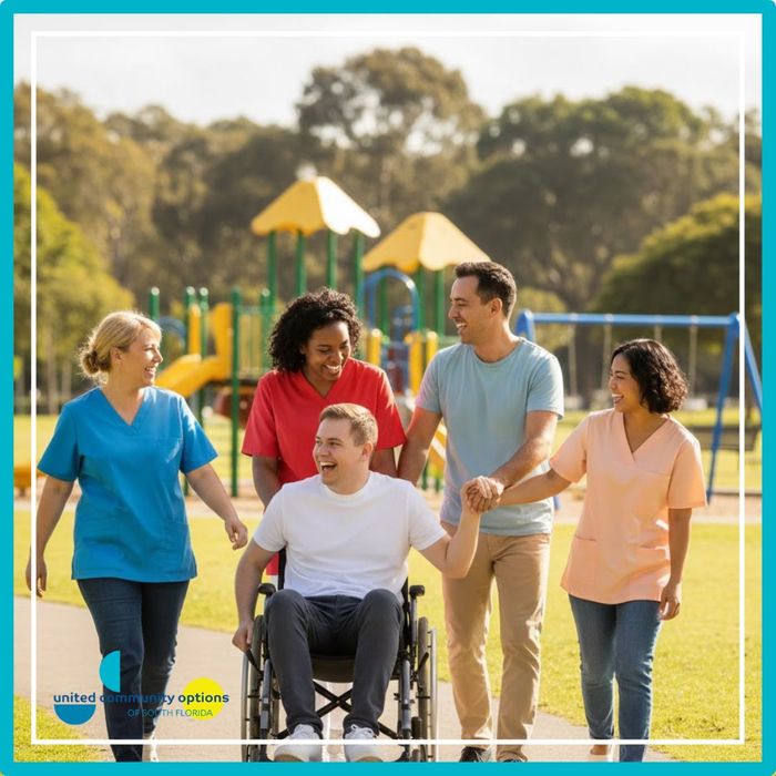 Group of diverse caregivers and an adult in a wheelchair enjoying a walk together in a park with a playground in the background