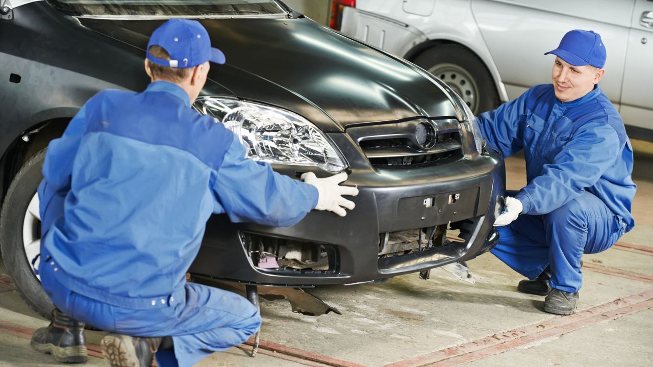 Two men replacing a bumper on a car