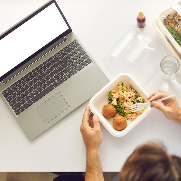 A perons eating lunch at their workdesk. A perons eating lunch at their workdesk.