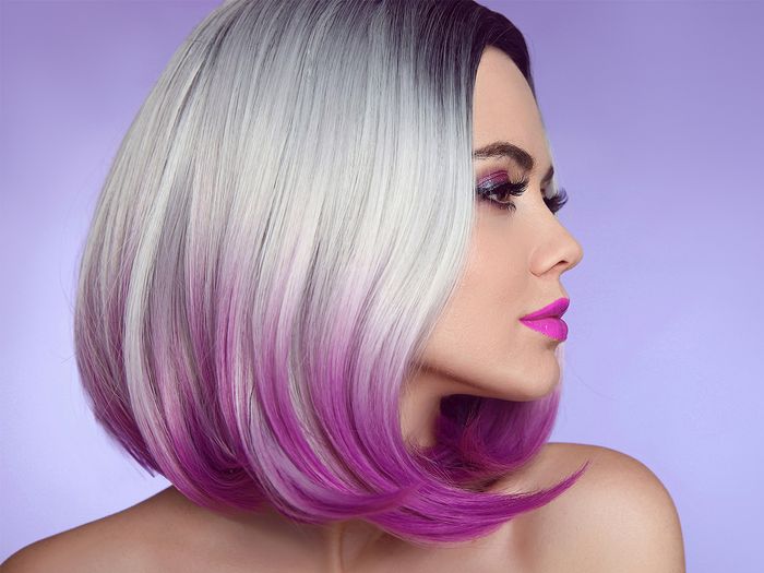 Close up profile photo of a woman wearing a blonde bob wig with ombre pink tips, curled at the ends against a purple background.