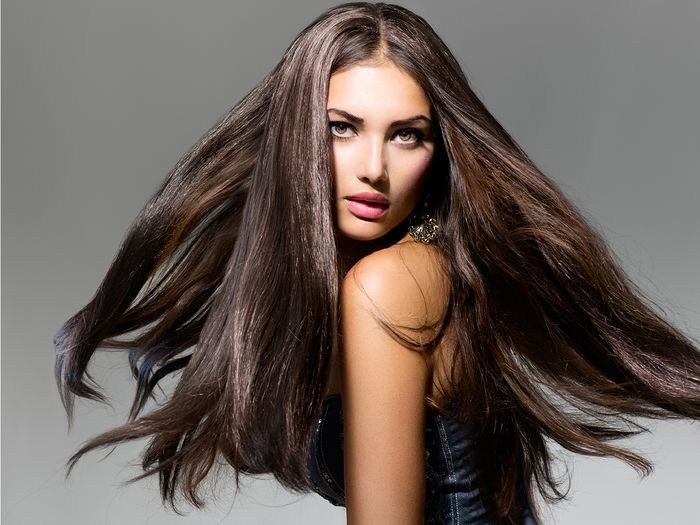 A female fashion model with long blowing hair against a dark grey background.