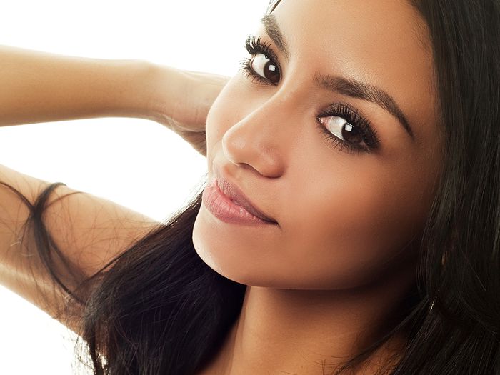 Close up portrait of a beautiful mixed race woman slightly smiling and posing with her arm behind her head.