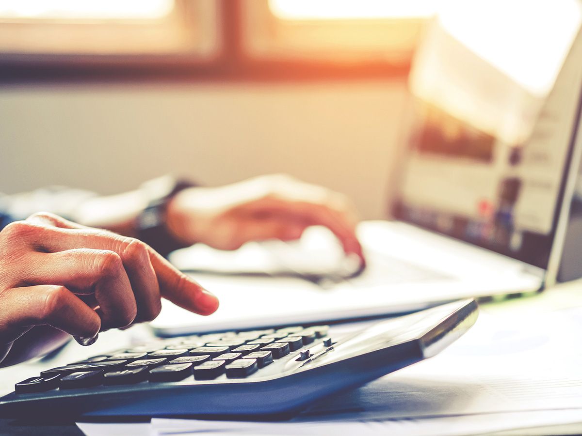 Image of a man typing on a calculator looking at a computer