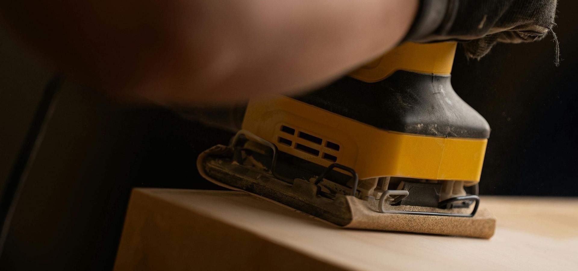 woodworker using an orbital power sander to create a smooth finish on a custom millwork project.