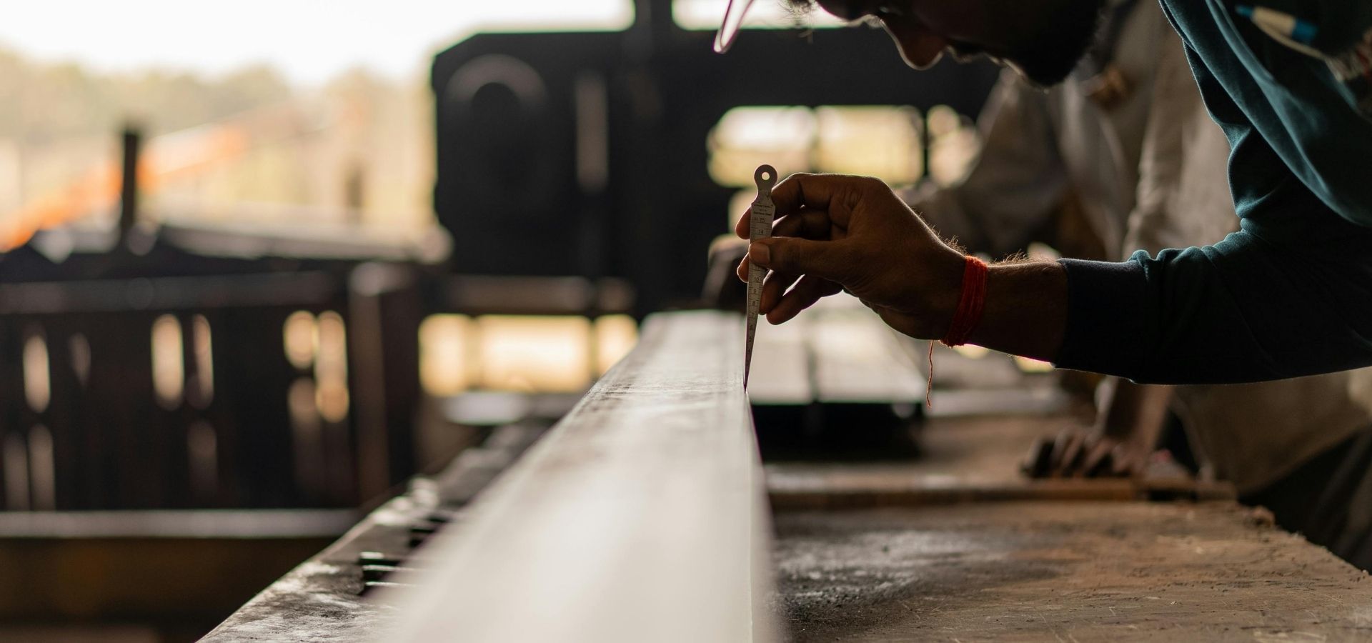 A professional carpenter using a precision marking gauge to measure a wood beam in a workshop with shallow depth of field.