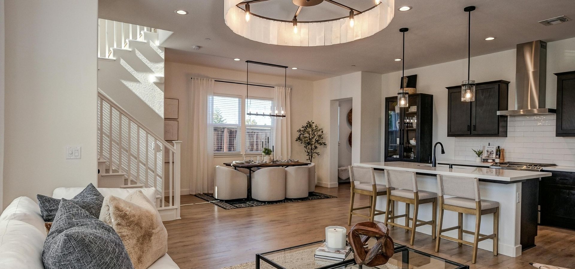 High-end residential interior featuring a modern kitchen with a large white island, dark cabinetry, and a spacious open-concept living area with a designer circular chandelier