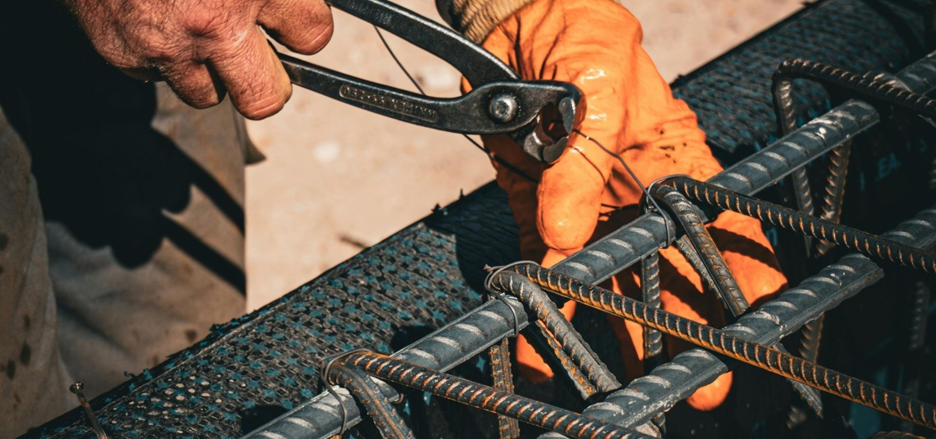 Close-up of a commercial construction worker using specialized tools to secure steel rebar for a concrete foundation.