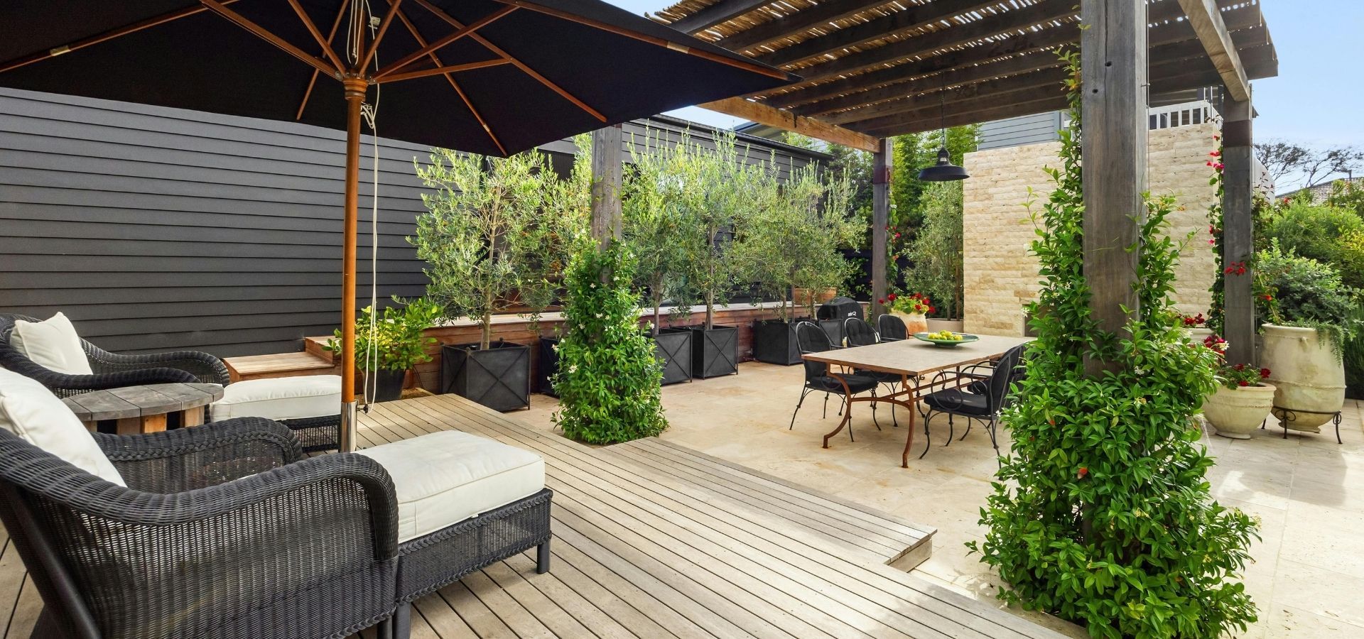 Luxury outdoor living space featuring a high-end wood deck, a modern pergola with integrated lighting, and premium wicker lounge chairs overlooking a dining area.